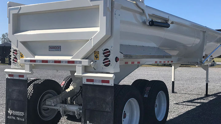 A white half-round dump trailer with the Hardox In My Body logo getting ready to hit the road