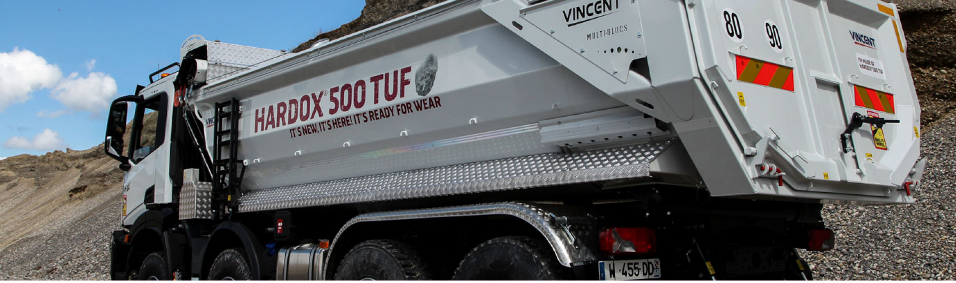 Kipperfahrzeug auf einer Baustelle mit Karosserie aus Hardox® 500 Tuf Stahl und dem Slogan „It’s New, It’s Here, It’s Ready for Wear!“