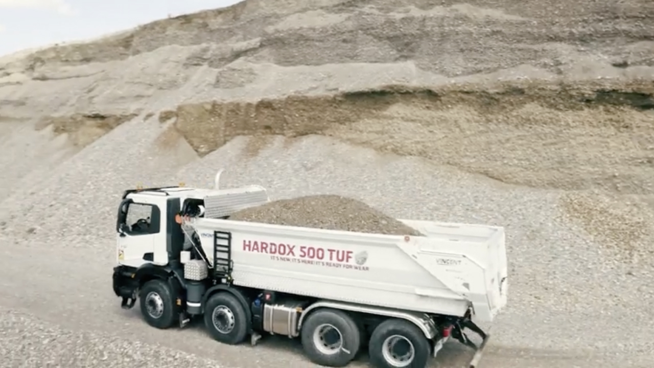 Một chiếc xe tải khai thác đang chở những tảng đá thô ráp, với thùng xe mang logo thương hiệu Hardox® 500 Tuf.