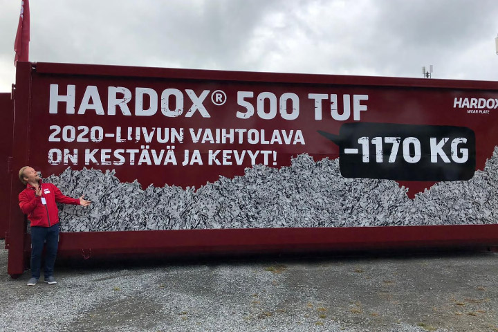 A bright red steel container in the forest, made in Hardox 500 Tuf steel, with Finnish wording. 