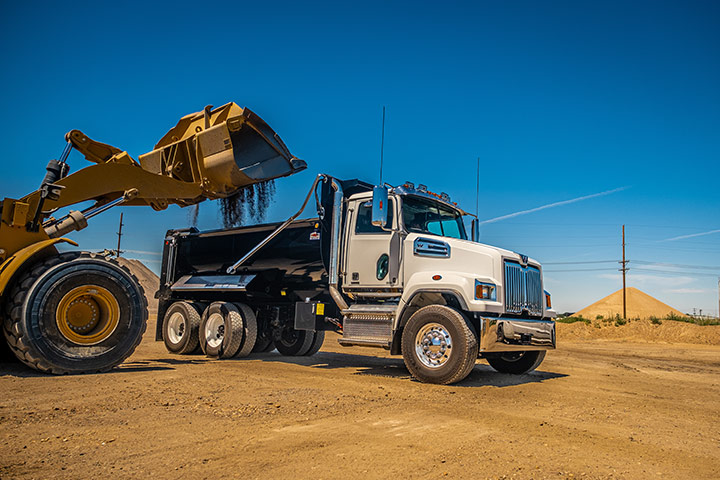 Truck with a black dump body being filled with abrasive material.