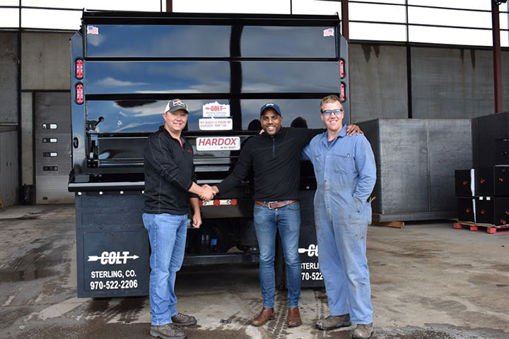 ชายที่กำลังยิ้มสามคนยืนหน้ารถดัมพ์แบรนด์ Colt คันแรกที่ผลิตโดยใช้ Hardox® 500 Tuf จาก Industrial Welding Supply 