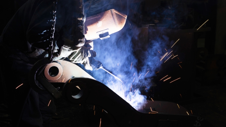 A welder with hardhat on against a dark smoky background.