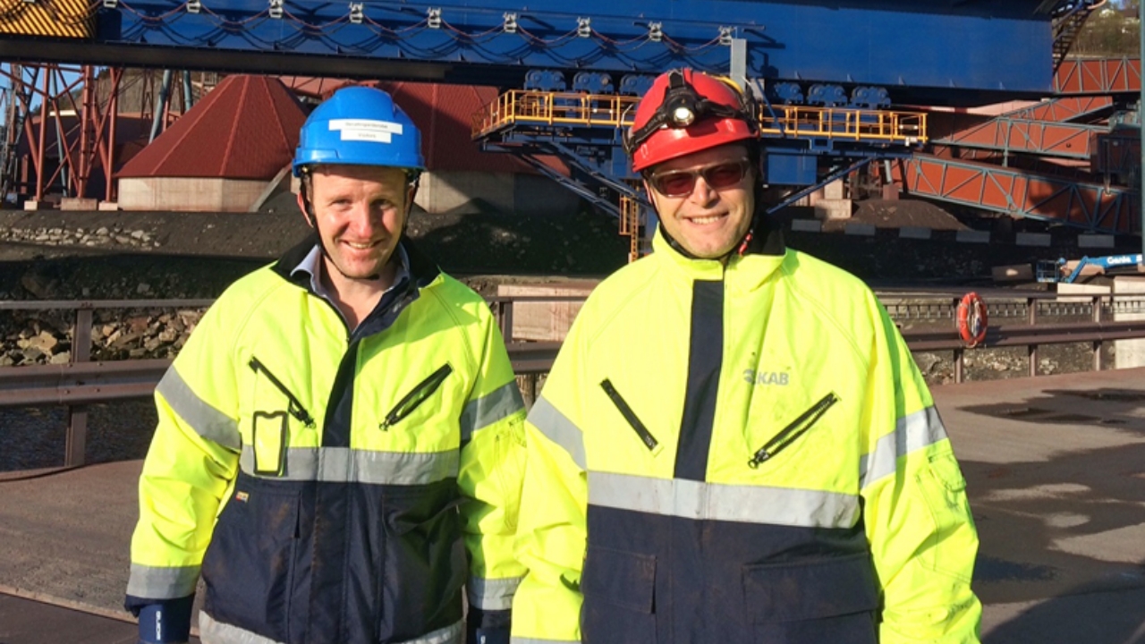 Two smiling employees in hardhats at Narvik harbor in Sweden. 