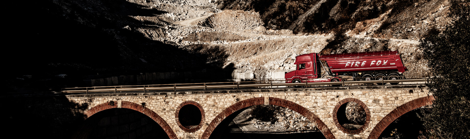 Một chiếc xe tải Fire Fox màu đỏ rực được làm bằng thép tấm Hardox 500 Tuf đang băng qua một cây cầu