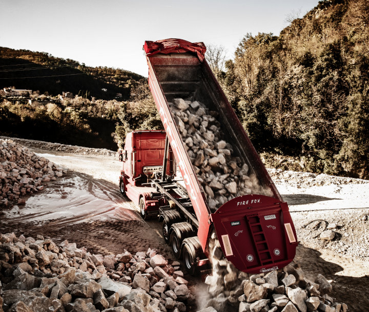 Camion ribaltabile Fire Fox rosso brillante realizzato in lamiera antiusura Hardox mentre scarica roccia abrasiva