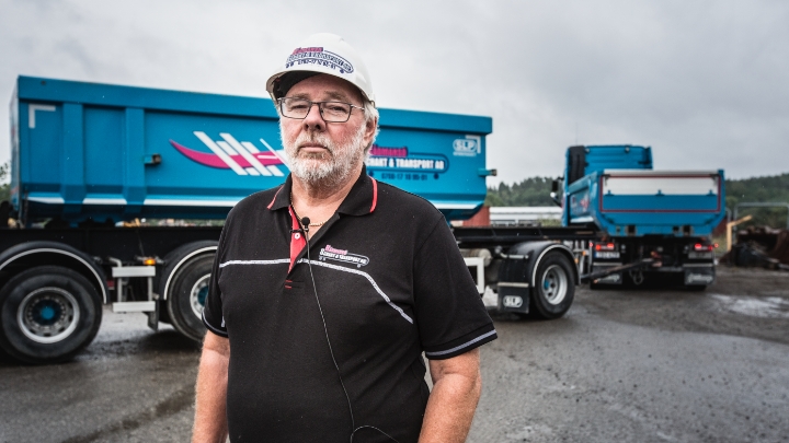 Ларс Эрикссон, сотрудник транспортной компании Rådmansö, стоит перед голубыми прицепами, платформы которых изготовлены из стали Hardox® 500 Tuf.