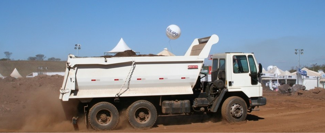 A white dump truck with body made in Hardox® 500 Tuf steel travelling along a dirt road against a clear blue sky.