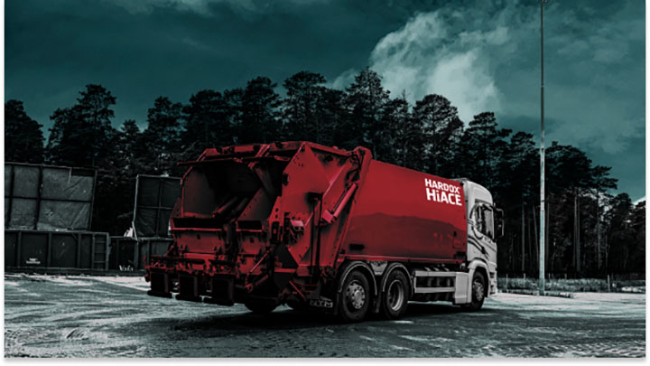 Mélyvörös színű hulladékszállító teherautó Hardox® Hi Ace korrózióálló acélból készült felépítménnyel.