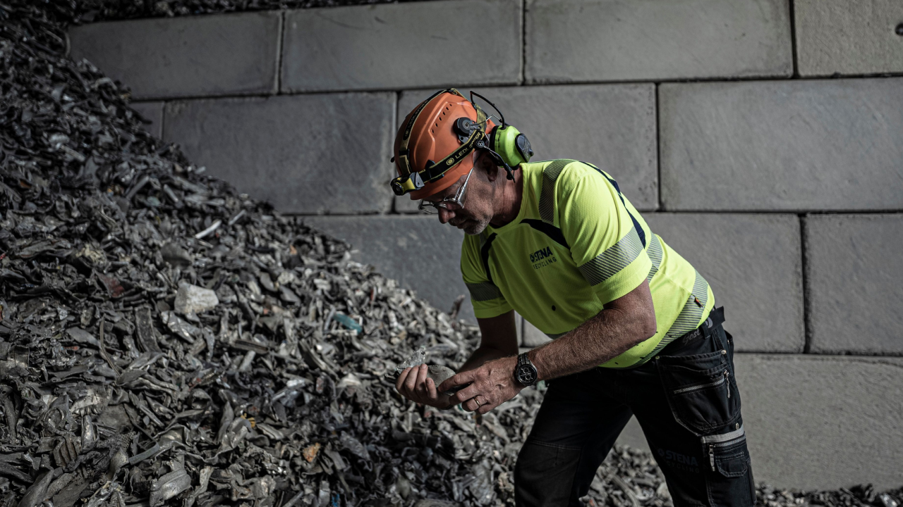 A man inspecting a pile of waste and scrap shards at a recycling plant.