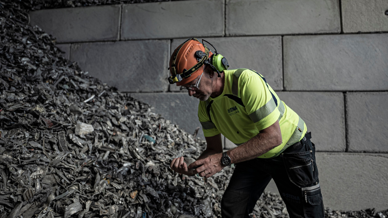 Muž kontrolující hromadu odpadu a střepů v recyklačním podniku.