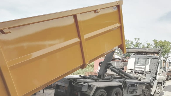 부식에 강한 강재로 제작된 밝은 노란색 폐기물 컨테이너 적재함을 기울이고 있는 덤프 트럭.