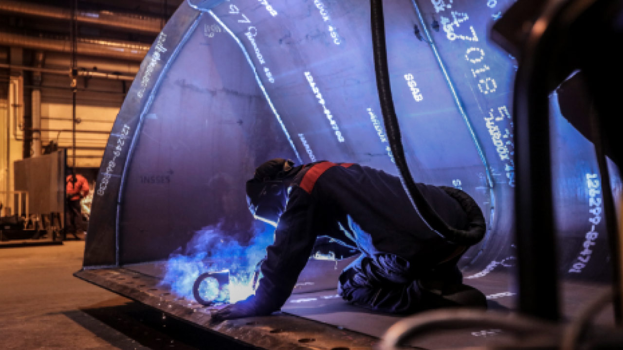 Un saldatore intento a saldare all'interno di un'enorme benna per escavatore realizzata in lamiera d'acciaio Hardox 400 resistente e dura.