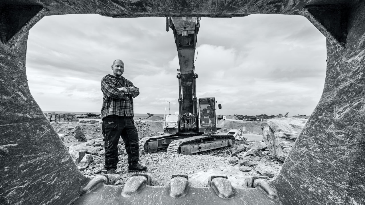 Munkaterületen álló, Hardox 400 kopásálló lemezből készült hatalmas kotrókanál belsejébe néző munkás.