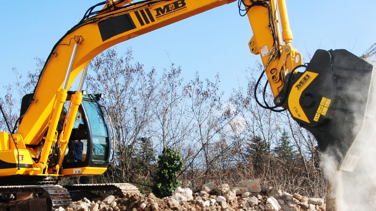 Un escavatore cingolato giallo che scarica rocce abrasive, con benna dell'escavatore in acciaio antiusura Hardox 400.