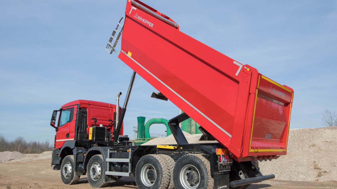 Um caminhão com carroceria feita com o aço Hardox® 450, passando por um canteiro de obras com uma carga de cascalho abrasivo e rochas.