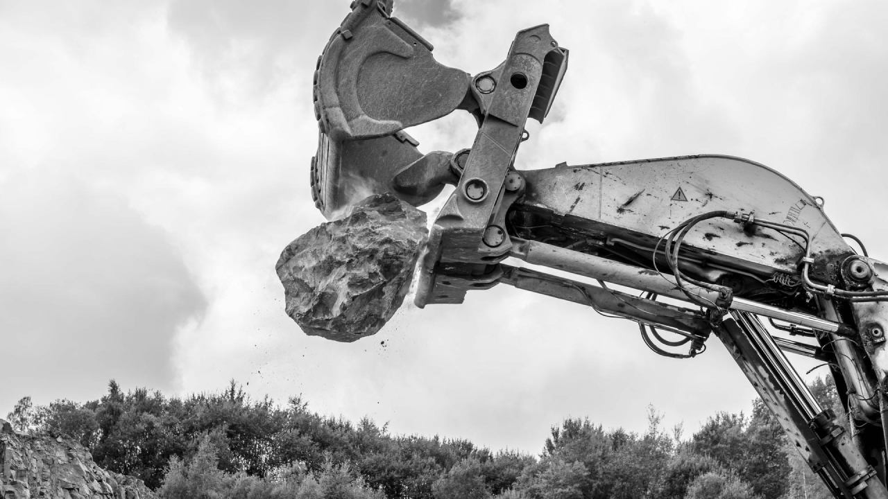 Excavadora gigante liberando una roca enorme en el aire. Los bordes de la pala son de acero Hardox® 450.