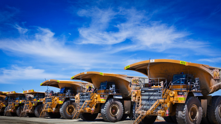 Rivi keltaisia kaivoskuorma-autoja kirkkaansinistä taivasta vasten. Lavat on valmistettu Hardox® 500 Tuf -teräksestä.