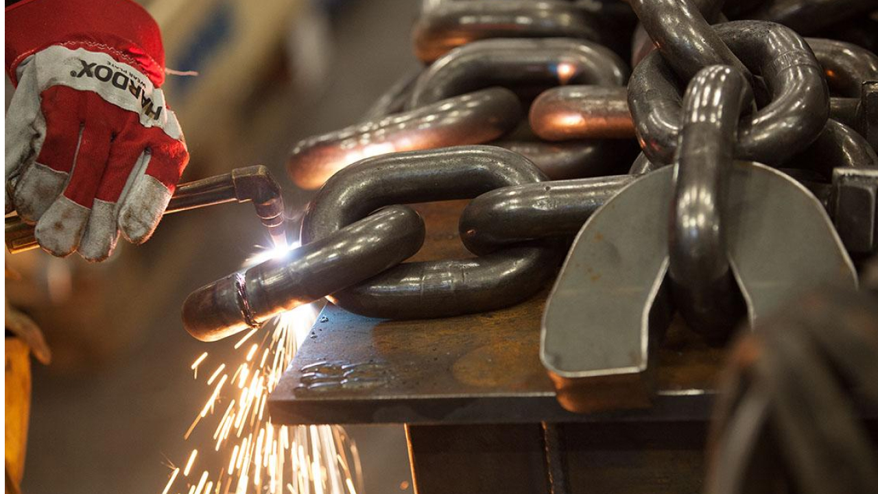 Nahaufnahme der behandschuhten Hand eines Schweißers, der an einer schweren Metallkette aus festem und zähem Hardox® Verschleißblech arbeitet. 