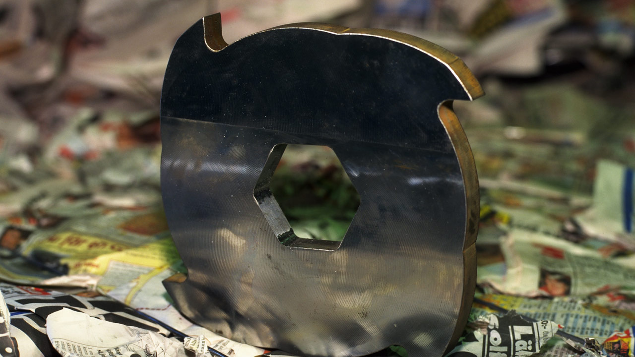 Közeli felvétel egy Hardox 600 extra-kemény acéllemezből készült aprító késről, amely papírhulladékot vág át egy újrahasznosító üzemben.
