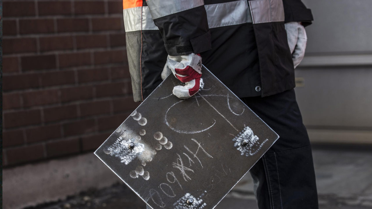 Hand eines Arbeiters, die ein bolzengeschweißtes Auskleidungsblech aus extrahartem Hardox 600 Blech hält.