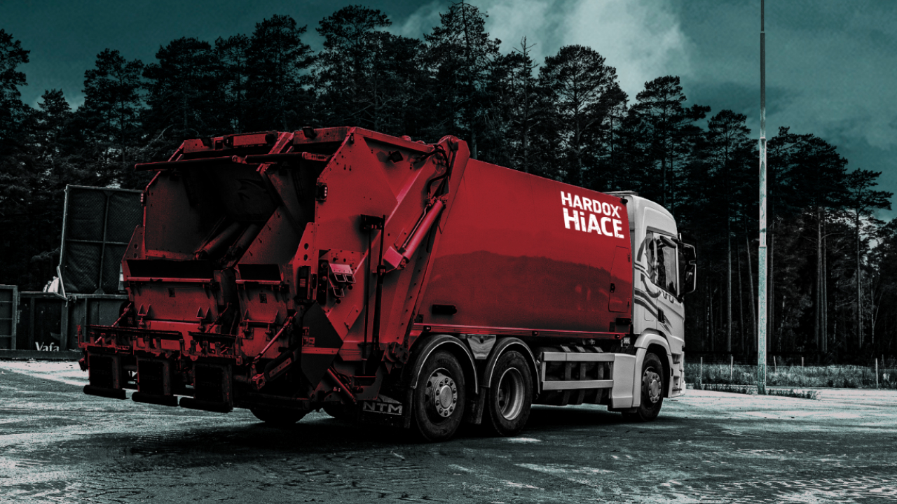 Um caminhão de lixo com a carroceria vermelha e a marca do aço Hardox® HiAce.