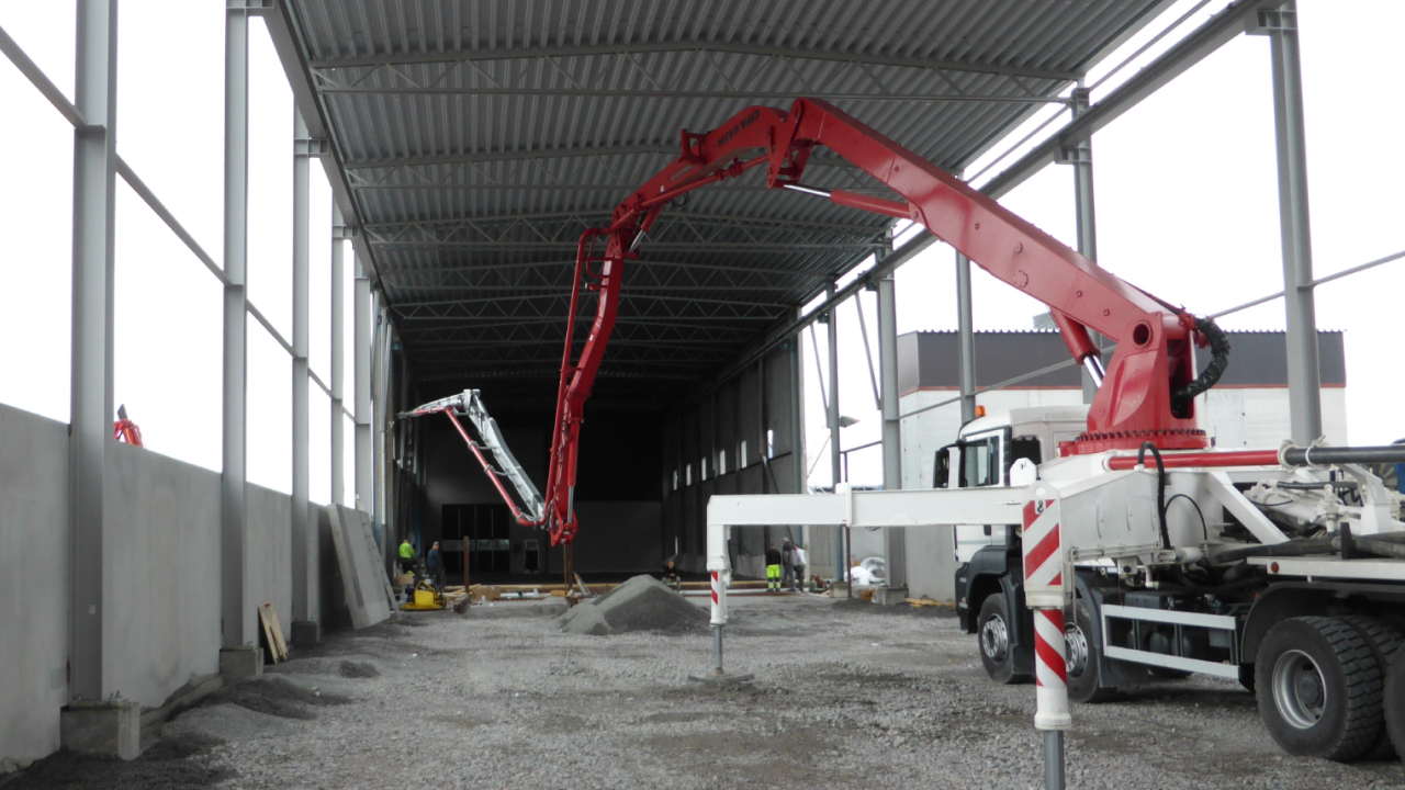 Un camion-pompe à béton avec des tubes en acier Hardox® résistant à l’abrasion en train de couler sur un sol en béton dans un bâtiment industriel