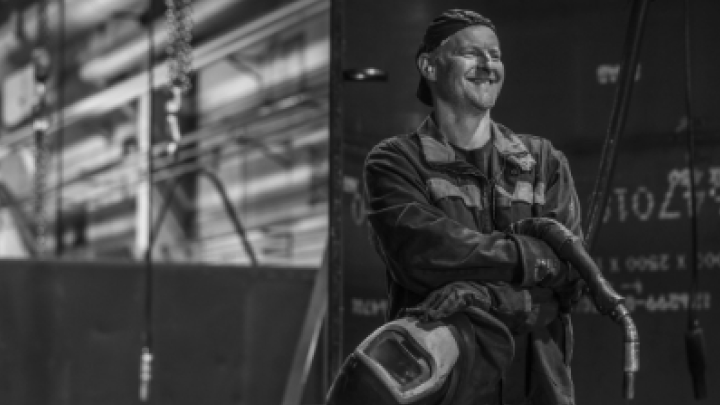 Fotografía en blanco y negro de un hombre sonriendo frente a tubos y tuberías de acero Hardox®