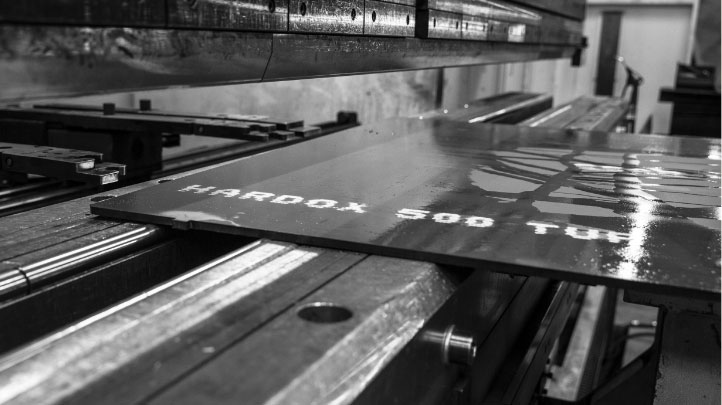 Fekete-fehér kép egy szuperszívós Hardox® 500 Tuf acéllemezről egy műhelyben.