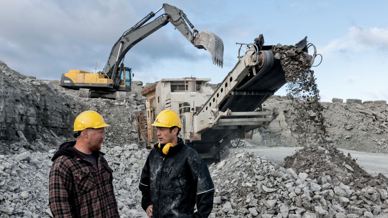 Hai người đàn ông đang đứng trước một số thiết bị khai thác đá có gắn phụ kiện làm bằng thép tấm AR cường độ cao, chịu mài mòn Hardox®. 