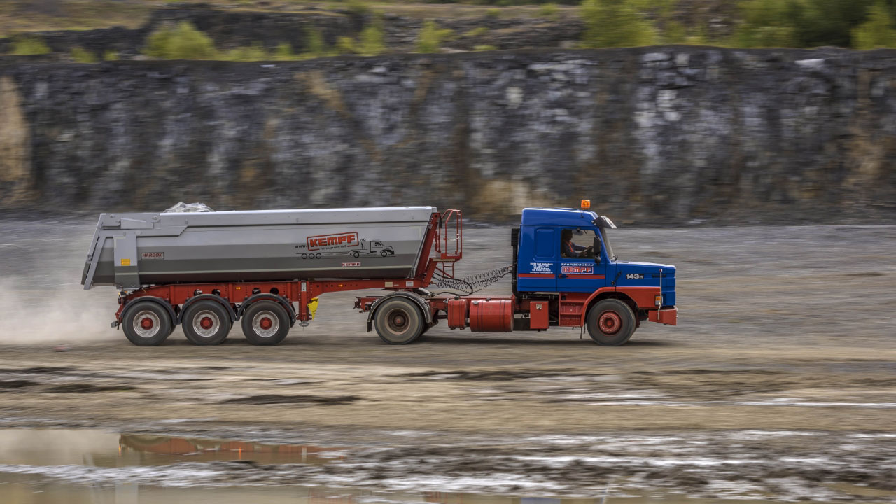 Lastbil och trailer på en grusväg, med flak i stark och seg Hardox® slitplåt för överlägsen slitstyrka och lång livslängd.