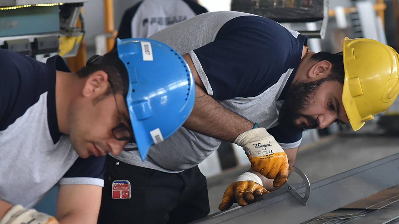 Dos hombres con cascos en el taller, fabricando una pieza de acero de alta resistencia Strenx®.