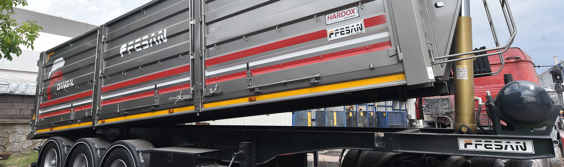 A shiny gray and red semitrailer dumper with the Fesan and Hardox® in My Body logos.