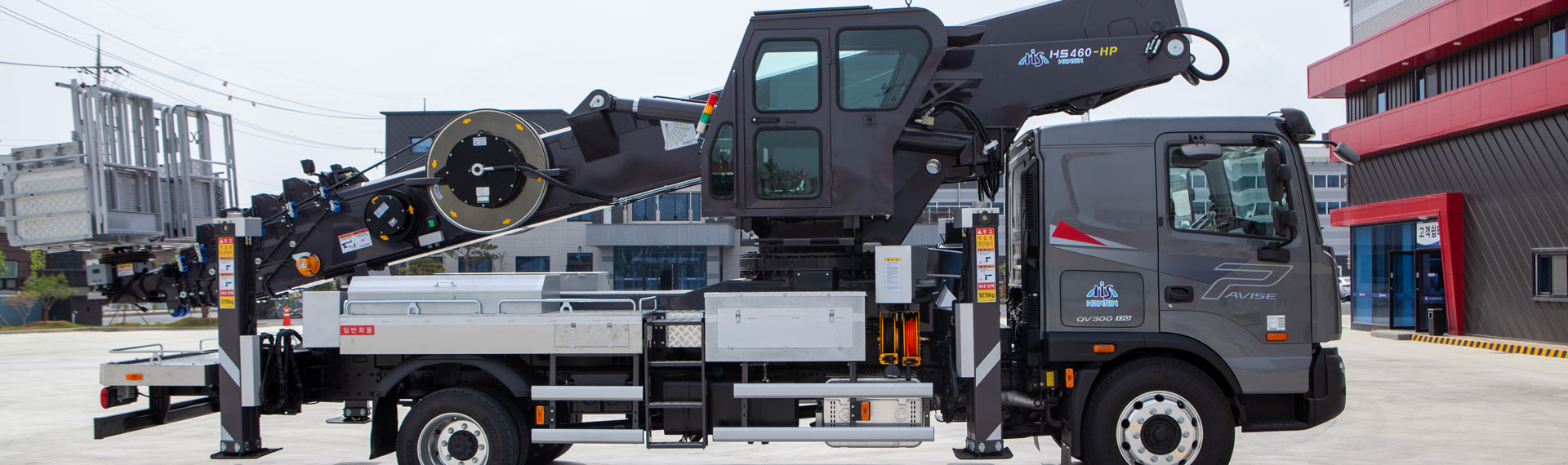 Vista laterale di un carrello elevatore aereo del produttore coreano Hansin, con braccio ripiegato extra-lungo e resistente in acciaio Strenx®.