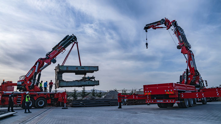 Два ярко-красных крана со стрелами из конструкционной стали Strenx, предназначенные для подъёма тяжелых грузов.