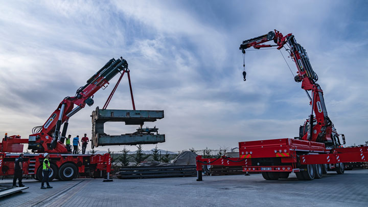 Deux grues rouge vif pour le levage de charges lourdes. Les flèches sont en acier structurel Strenx.