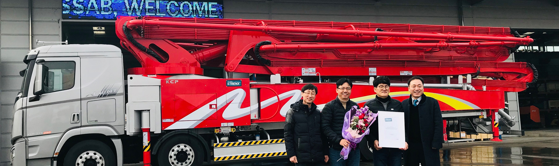 Camion-pompe à béton rouge vif avec des salariés de KCP fiers d’être titulaires d’un certificat my Inner Strenx