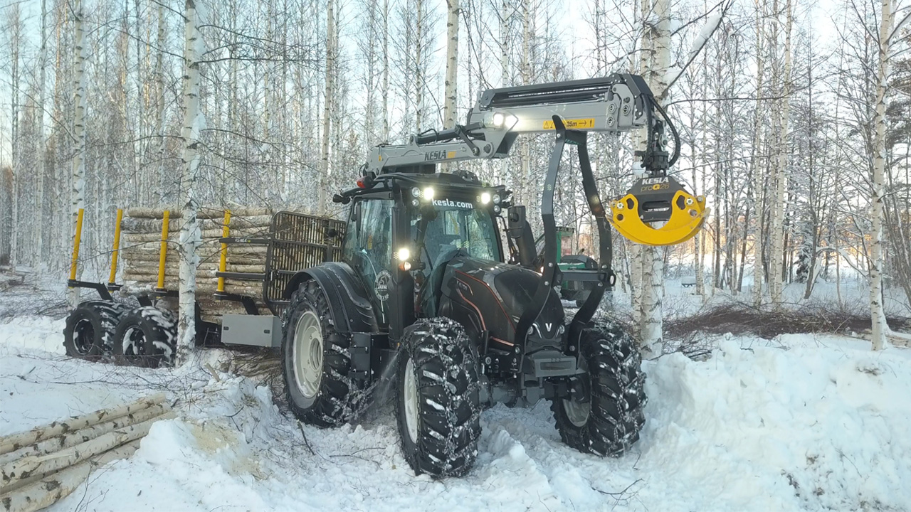 Tracteur avec grue en acier Strenx® ramassant des grumes dans une forêt en hiver.